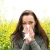 A woman blowing her nose, suffering from allergies.