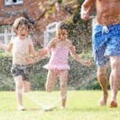 A family playing in a sprinkler.
