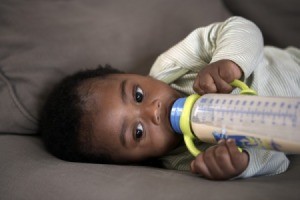 Baby drinking a bottle on a sofa.