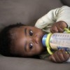 Baby drinking a bottle on a sofa.