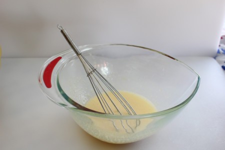Egg and sugar mixture in glass bowl with whisk.