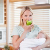 A woman eating an apple with her baby.