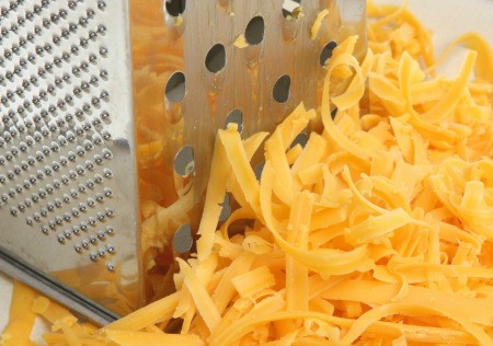 A cheese grater and a pile of grated cheese.