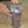 Wrapping yarn around a glass vase.