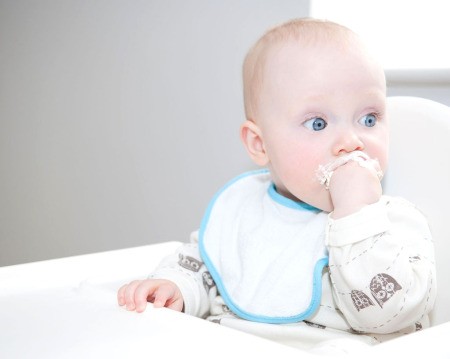 Baby wearing bib and sucking on her fingers.