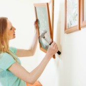 A woman hanging pictures frames on a wall.