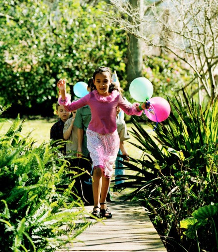 A birthday girl running with balloons in a garden.
