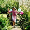 A birthday girl running with balloons in a garden.