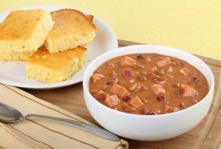 A bowl of ham and bean soup with corn bread.