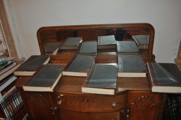 Volumes lying on an antique cabinet with low mirrored back.