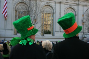 Two people watching a St Patrick's Day parade.