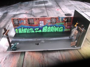 This handmade diorama is an urban street scene with telephone polls, brick walls with windows and graffiti.