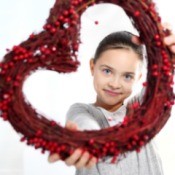 A girl holding a red heart wreath.
