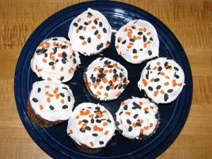 A plate of pumpkin cupcakes with black and orange sprinkles.