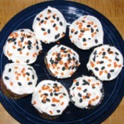 A plate of pumpkin cupcakes with black and orange sprinkles.