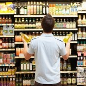 A man looking at a rack of different types of oil at a supermarket.