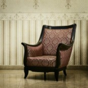 An antique chair in a room with expensive looking wallpaper.