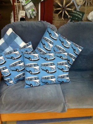 Four cushions or throw pillows. Three have VW microbus motif and one is blue plaid.