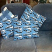 Four cushions or throw pillows. Three have VW microbus motif and one is blue plaid.
