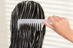 A woman combing conditioner into her hair.