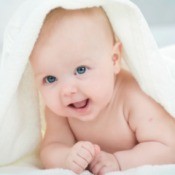 A smiling baby under a white blanket.