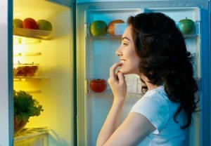 A woman looking in her refrigerator at night.