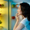 A woman looking in her refrigerator at night.