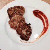 three croquettes on white plate with hot sauce on the side