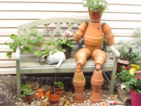 Terra cotta flowerpot man sitting on garden bench