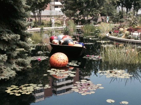 multicolored glass globes in a small wooden boat on pond with a large speckled orange ball floating nearby