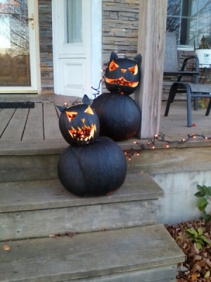 two black cat pumpkins made from a smaller carved face pumpkin on top of a larger one