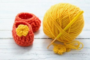 orange booties with yellow flower next to ball of yellow yarn with crochet hook