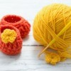 orange booties with yellow flower next to ball of yellow yarn with crochet hook