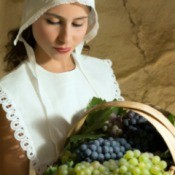 girl wearing a bonnet holding a basket of grapes