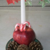 cored apple with candle and candy canes surrounded by pine cones