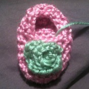 A crocheted rosebud on a baby bootie.