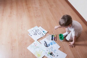 A child painting on laminate wood flooring.