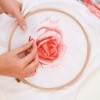 woman cross stitching a rose