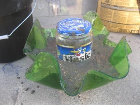 A recycled jar in the middle of a bowl filled with concrete.