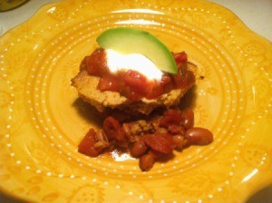 A dish of tamale pie, topped with salsa, sour cream and avocado.