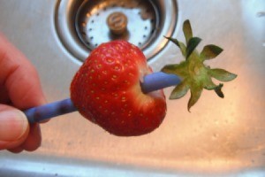 A strawberry with a straw used for removing the tops.