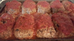 A row of baked meatloaves topped with tomato sauce.