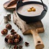 cast iron pot of soup with chestnuts scattered about