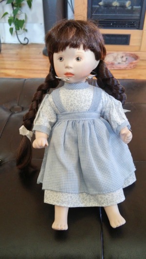 dark haired doll wearing white dress with a blue pinafore over it