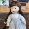 dark haired doll wearing white dress with a blue pinafore over it