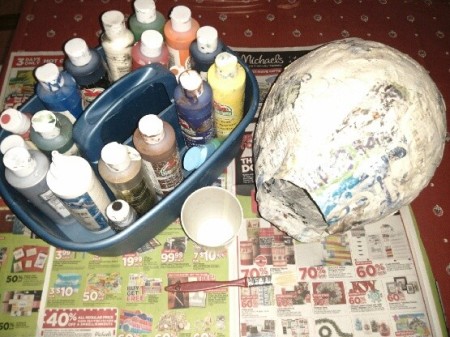 A paper-maché covered balloon next to paints.