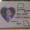 A wooden frame with a heart shaped opening, decorated with two state outlines and a quote.