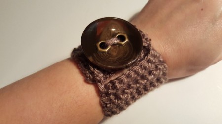 A crocheted bracelet with a large brown button.