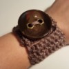 A crocheted bracelet with a large brown button.