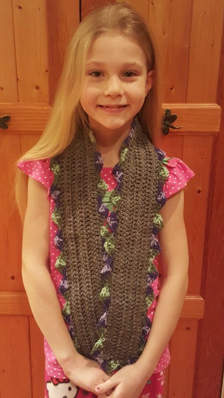 A girl with a brown crocheted scarf with a scallop patten.